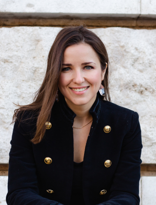 Mindset coach Monika Lerch sitting in front of a wall, looking and smiling directly into the camera.